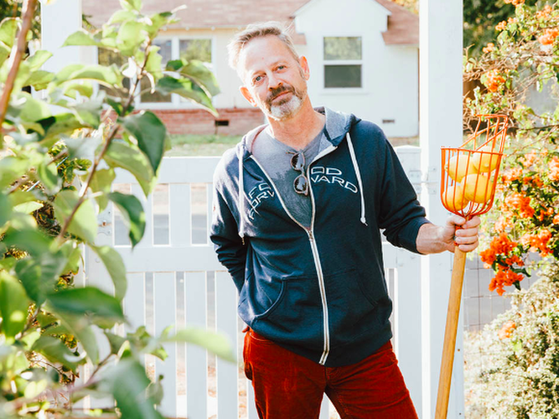Food Forward's CEO stands with a fruit picker and lemons.