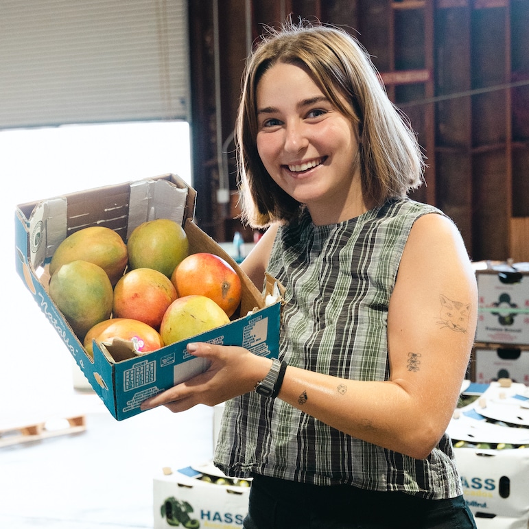 Natalie smiling and holding a box of mangoes at The Sprout